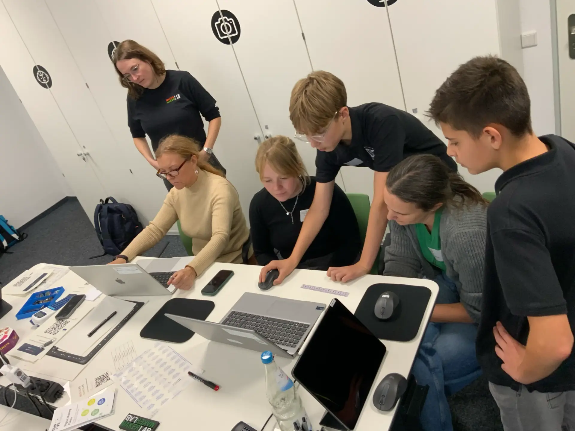 Schüler erklären Lehrkräften während eines Workshops ein Programm am Laptop