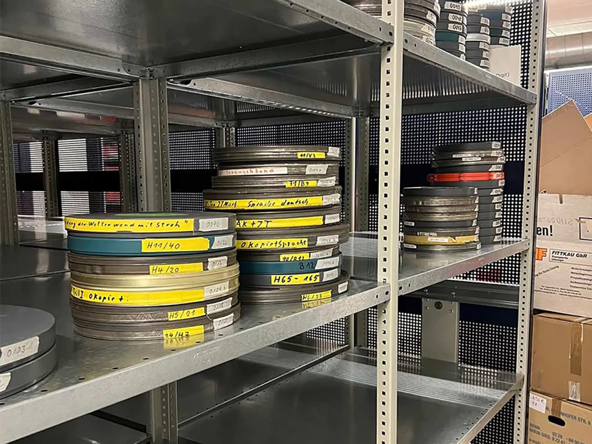 In einem Stahlregal sind analoge Filmrollen aus Metall aufeinander gestapelt