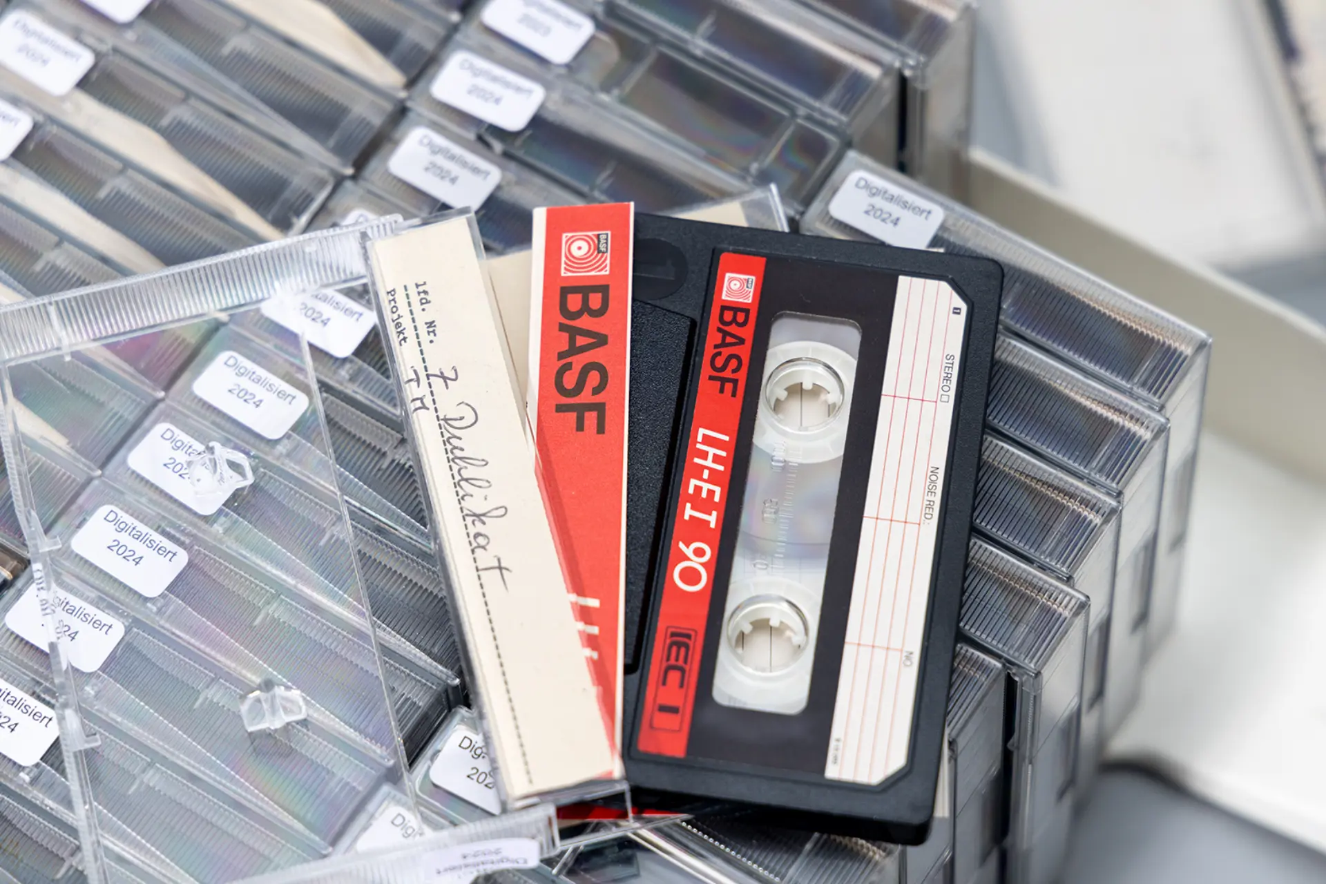 Eine klassische transparente Kassettenhülle mit Kassette liegt auf weiteren, gut sortierten Kassetten.
