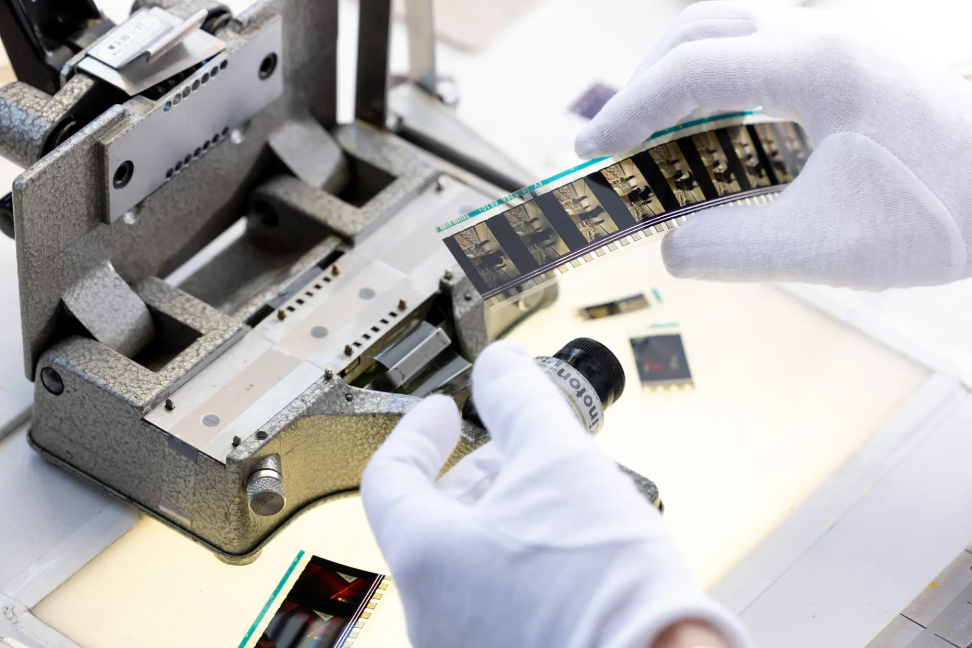 Person mit weißen Handschuhen hält analogen Filmstreifen an einem Filmscanner zur Digitalisierung.