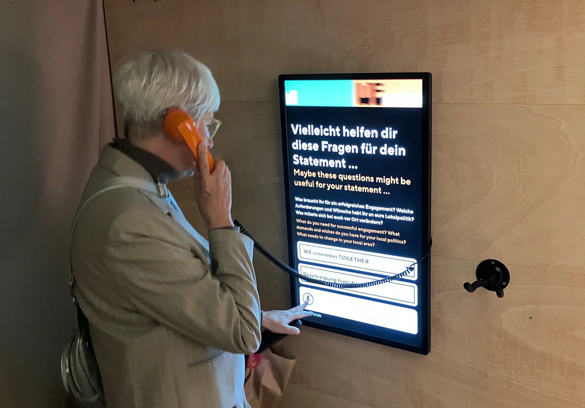 Person nutzt eine interaktive Audiostation mit Telefonhörer und Touchscreen, um ein Statement zu lokalpolitischen Themen aufzunehmen.