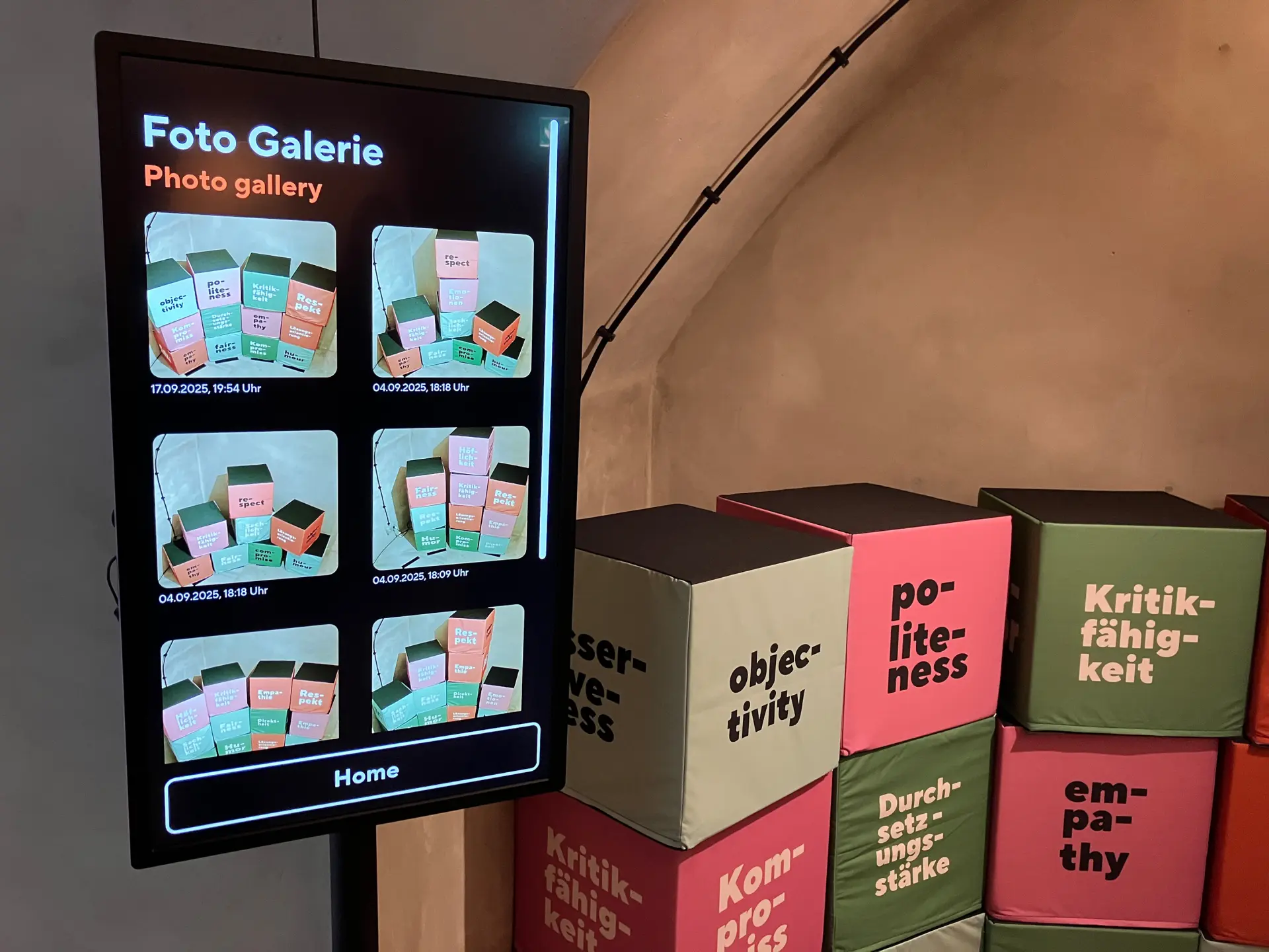 Digitales Display mit der Aufforderung „Ordne die Würfel neu an!“ und bunten Begriffswürfeln zu Werten wie Humor, Respekt, Empathie und Fairness.