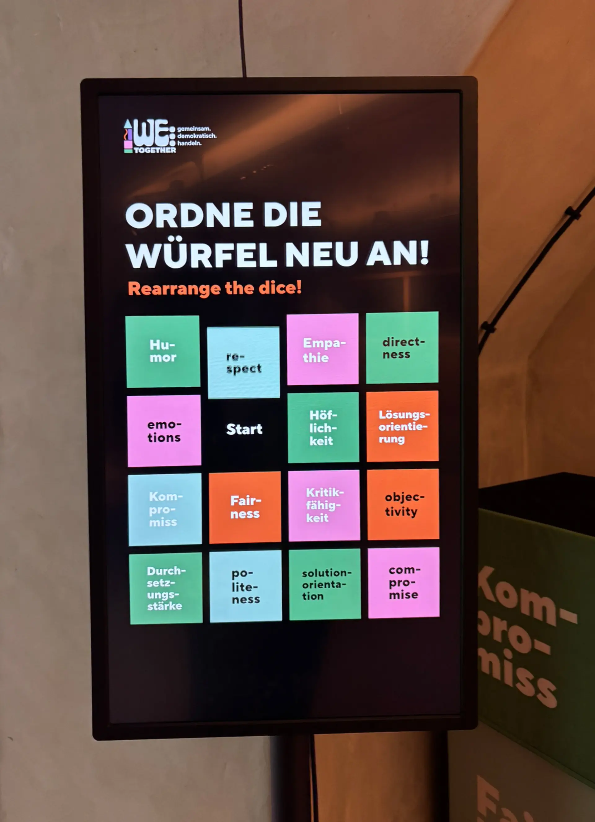 Digitales Display mit der Aufforderung „Ordne die Würfel neu an!“ und bunten Begriffswürfeln zu Werten wie Humor, Respekt, Empathie und Fairness.