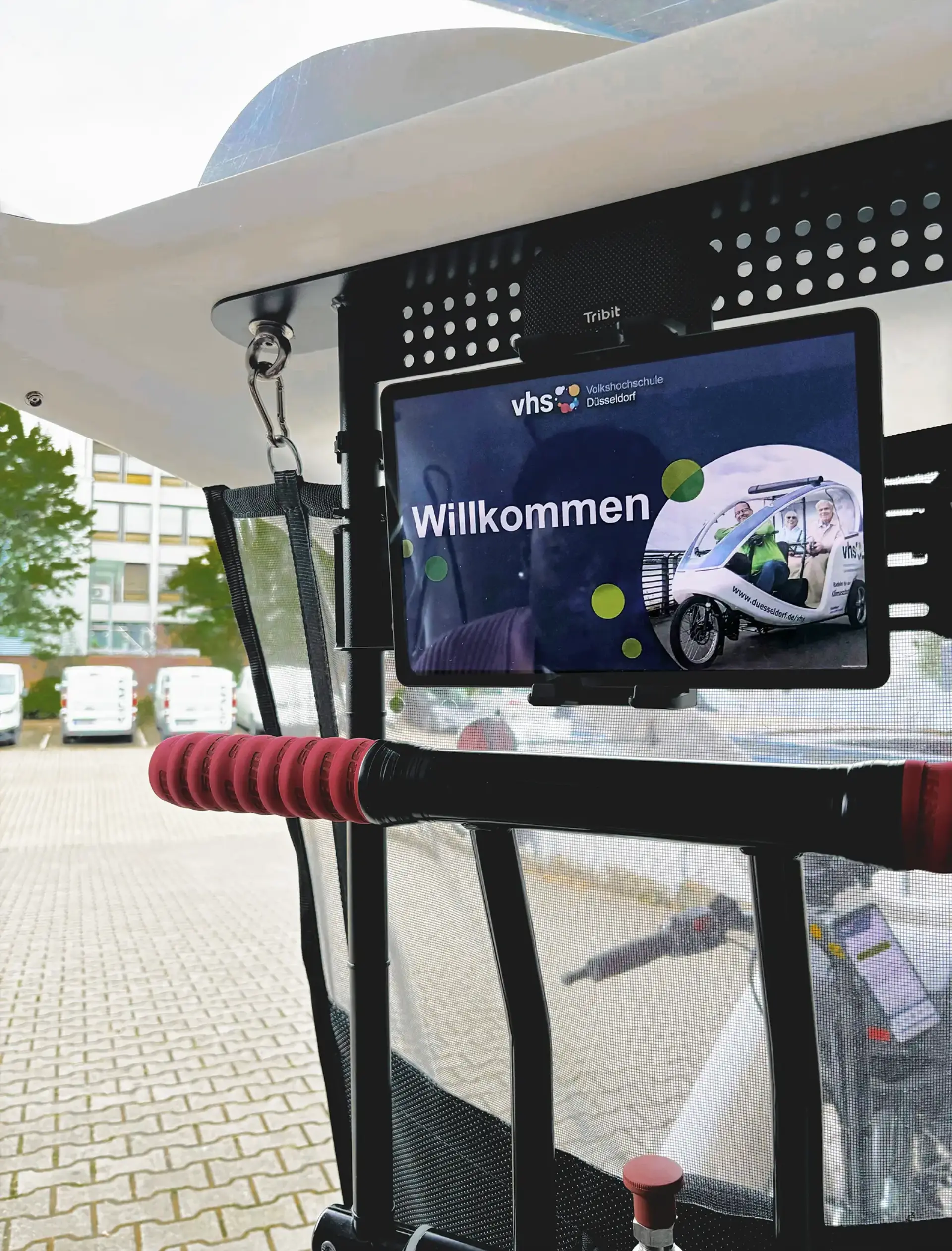 Tablet mit Begrüßungsbildschirm der Volkshochschule Düsseldorf in einem überdachten Rikschafahrzeug