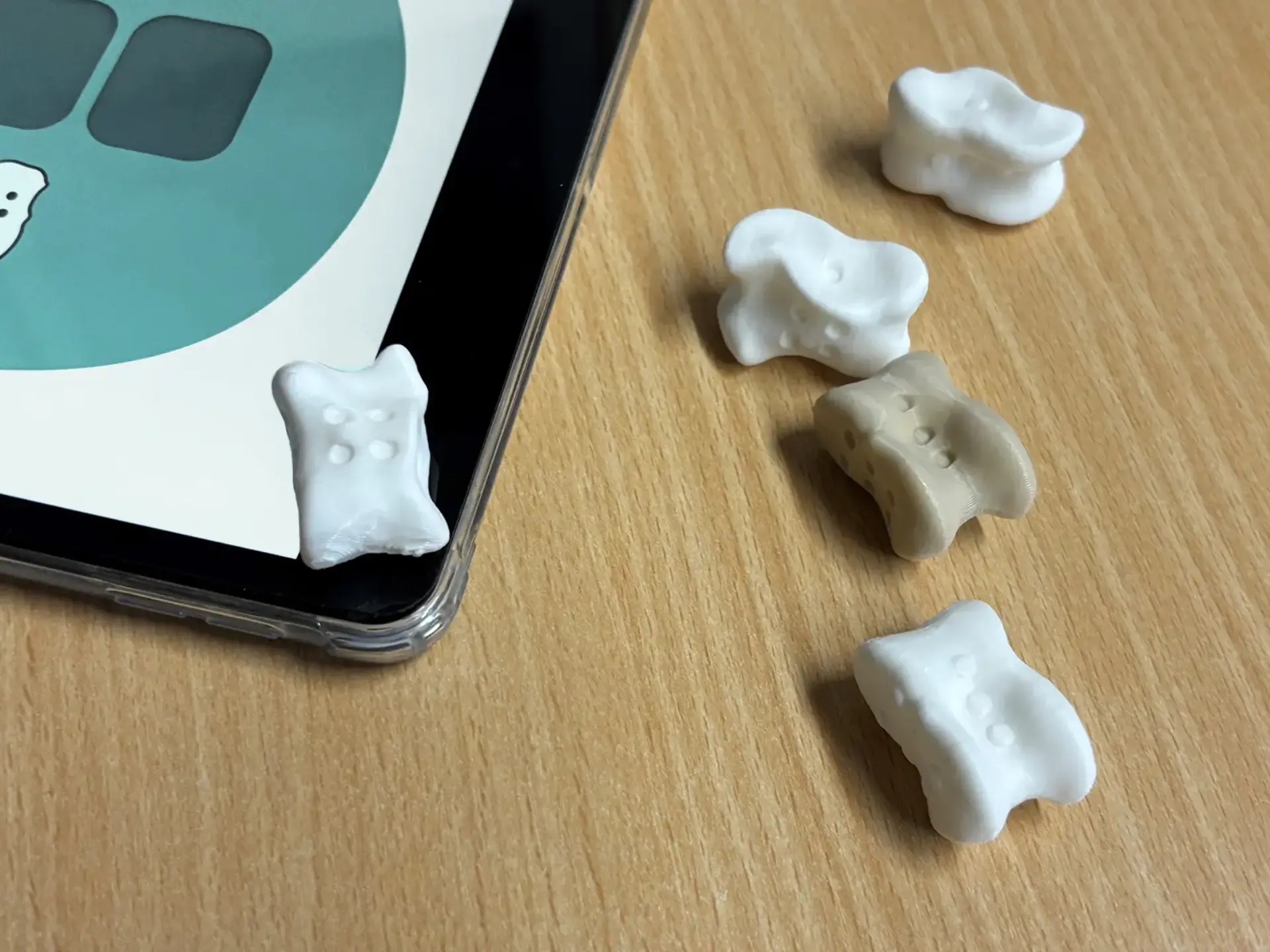 Nahaufnahme eines Tablets mit Lernspiel-App und mehreren kleinen Würfelfiguren auf einem Holztisch