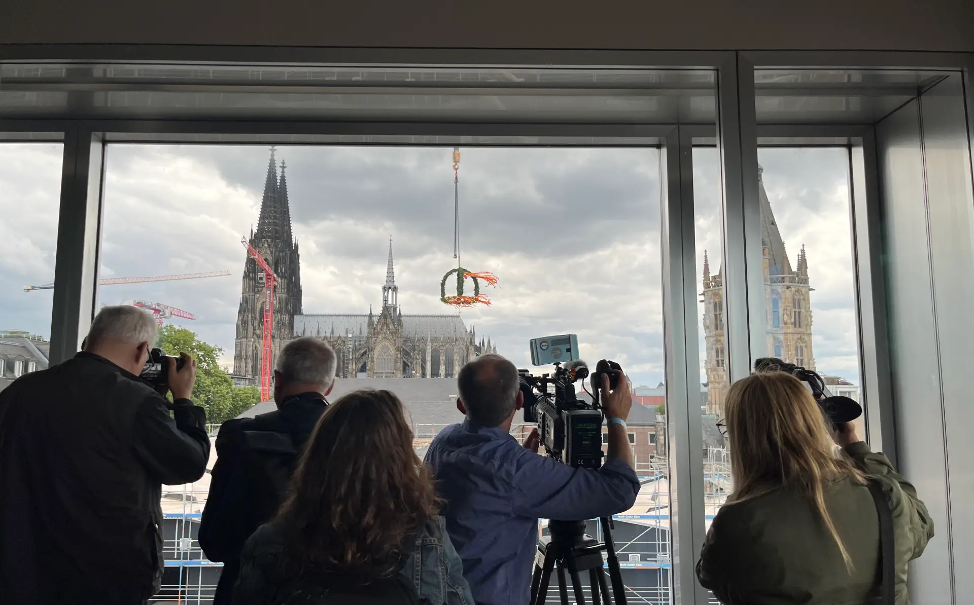 Ein Kameramann filmt aus dem Fenster einen Richtkranz vor dem Kölner Dom